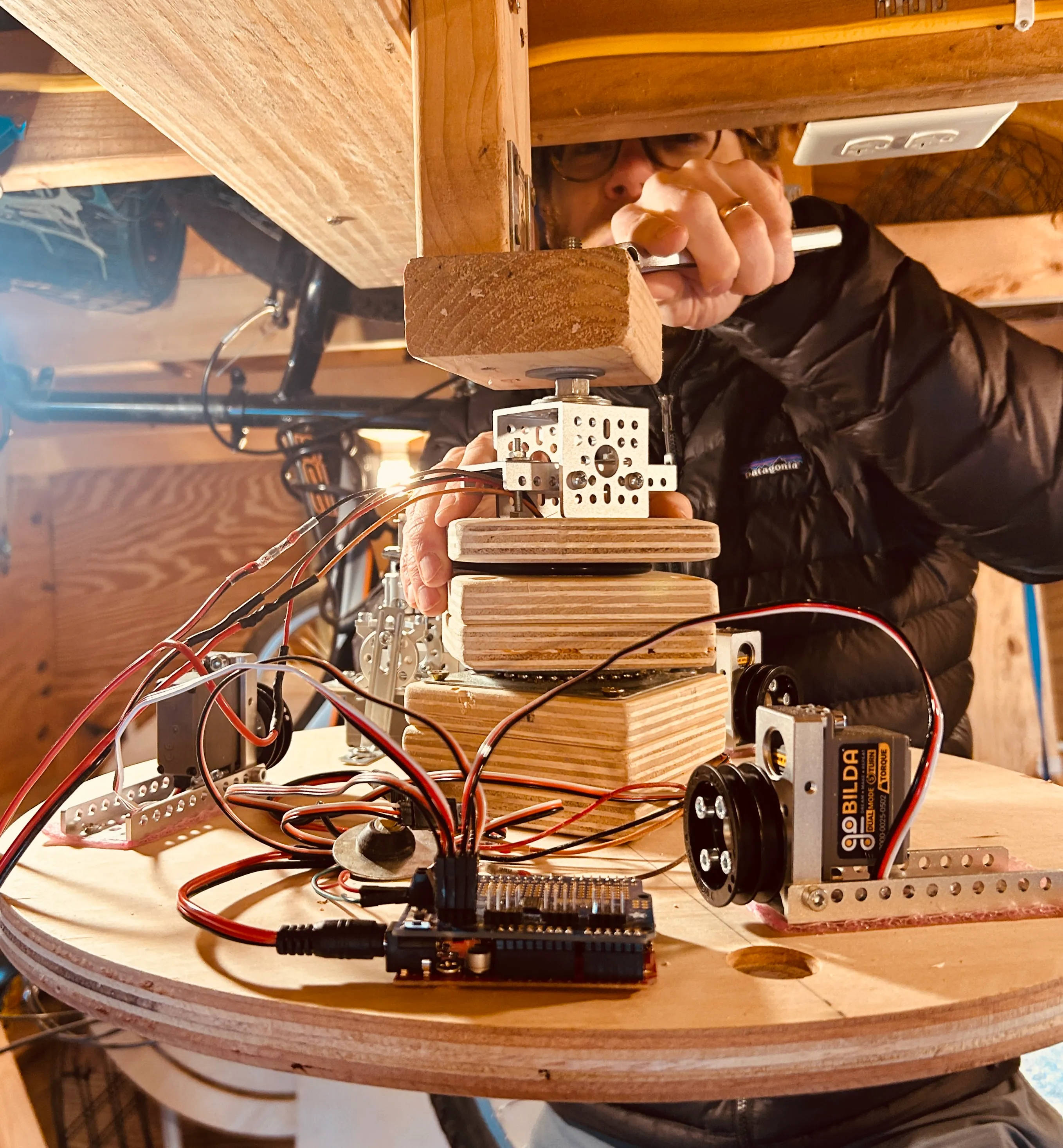 Close-up of hands assembling goBILDA servo motors, brackets, and an Arduino on the circular plywood base