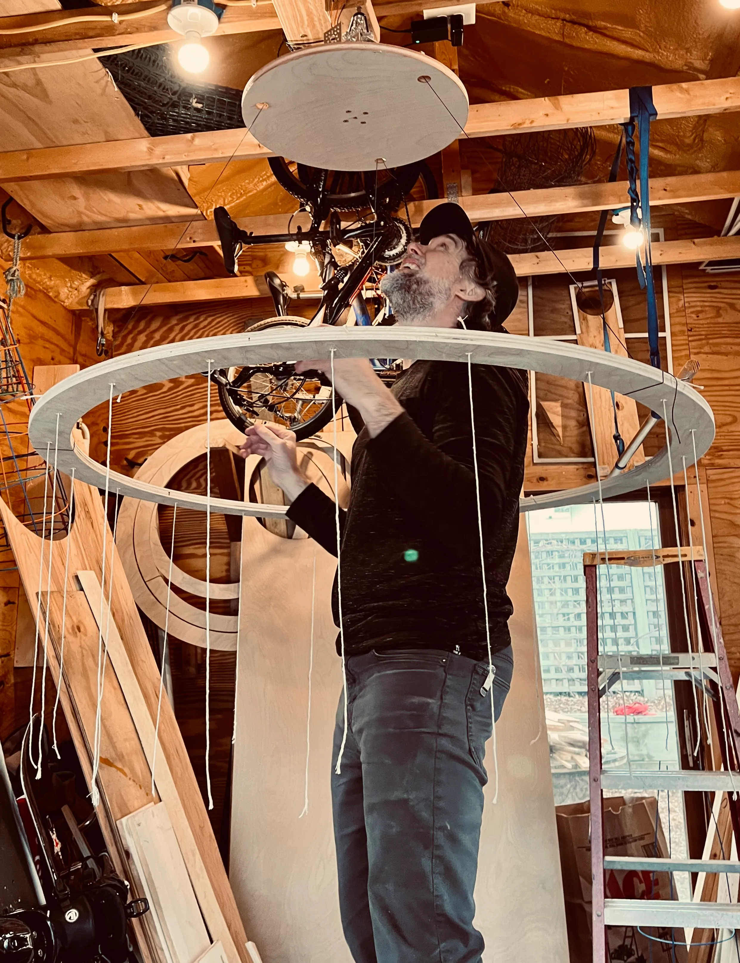 Tim standing beneath the suspended ring, attaching hanging strings to the structure