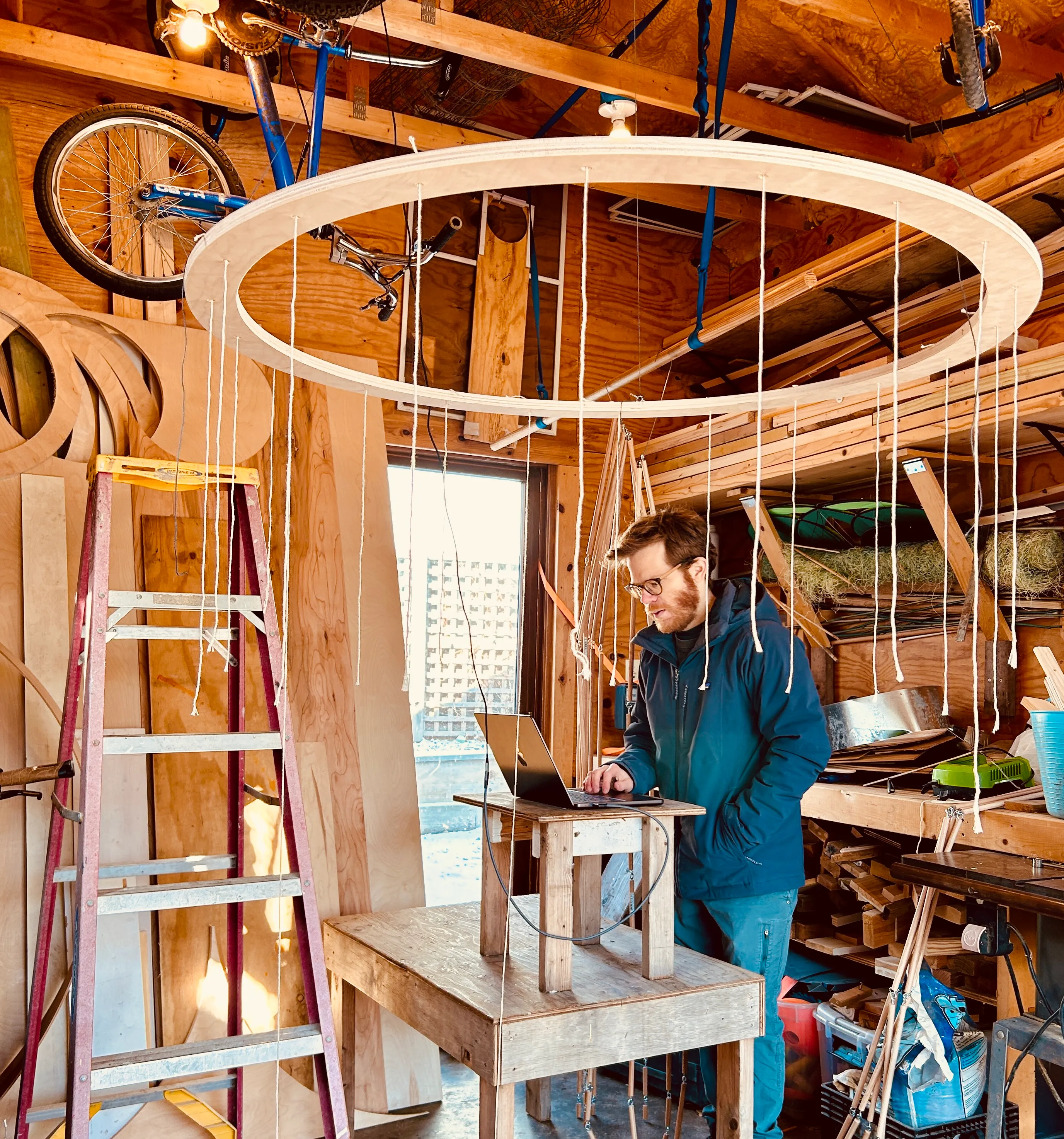 Tate programming at a laptop beneath the suspended ring with hanging strings