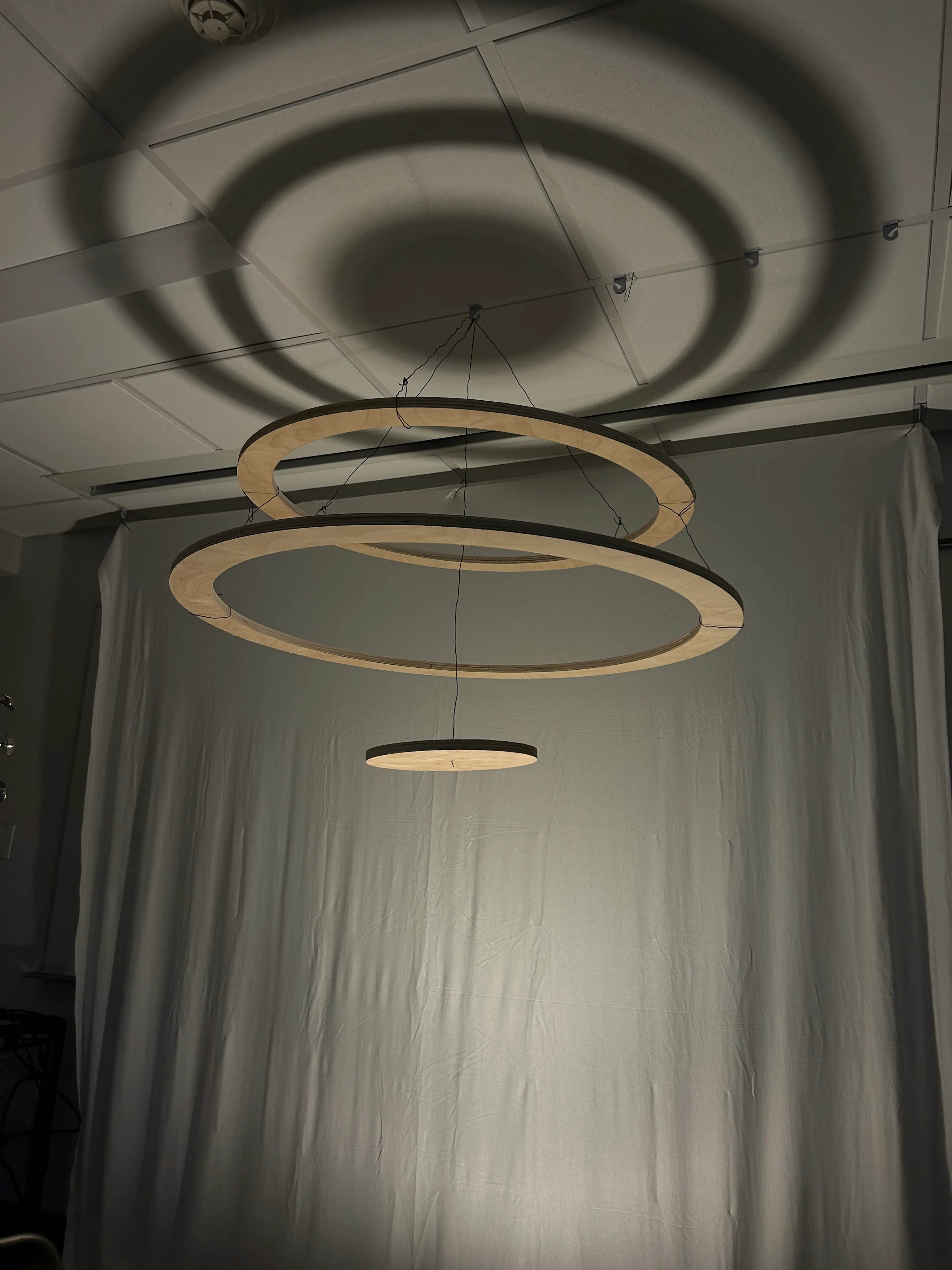 Suspended wooden rings casting concentric shadows during an early lighting test